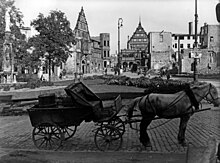 Blick mittig vom Marienplatz (Paderborn) in Richtung Rathausplatz. Die Zerstörung durch die Bombardierung ist klar sichtbar: Bis auf die Fassaden des historischen Rathauses und des Heising´schen Hauses sind alle Gebäude im Blickfeld zerstört. Im Vordergrund ein Pferdegespann.