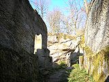 Gegenblick nach Nordosten mit dem Burgbrunnen unter dem Nordwestfelsen. In die Felswand sind Zulaufrinnen und Balkenlöcher der Brunnenstube eingearbeitet