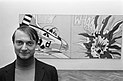 Schwarzweißfotografie Roy Lichtensteins in einem Ausstellungssaal vor seinem Gemälde Whaam!