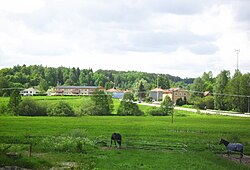 A far shot of the area. Very green field with a town in the distance. Many trees further than that.