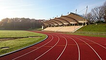 Foto des Stadions Gladbeck mit überdachter Tribüne, Laufbahn und Rasenfläche in der Morgensonne