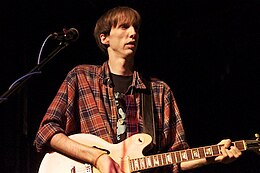 Photograph of a man in his twenties playing an electric guitar.