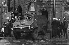 Das Schwarzweißfoto zeigt eine städtische Straßenszene, deren Zentrum ein gepanzerter Lkw mit Schriftzug POLITIE und niederländischem Kennzeichen bildet. Es handelt sich um ein zweiachsiges Fahrzeug mit grobstolligen Reifen; Fahrerhaus und restlicher Aufbau sind ineinander integriert. Lüftungsschlitze im unteren Bereich der Frontseite, zwischen den außen angebrachten Scheinwerfern, lassen auf einen vorn eingebauten Motor schließen. Die zwei Fenster vorn sind mit Schutzklappen versehen, die nach oben aufgeschwenkt sind. An der auf dem Foto ebenfalls sichtbaren linken Fahrzeugseite befinden sich nur kleine Sehschlitze. Auf dem Dach befindet sich ein kuppelartiger, ebenfalls gepanzerter Aufbau mit Sehschlitzen rundherum. Um das Fahrzeug herum stehen Personen mit weißen Schutzhelmen, vermutlich Polizisten. Die Vorderseite des Fahrzeugs ist durch Spritzer verschmutzt. Es ist so abgestellt, dass das Fahrzeugheck mit der Eingangstür eines dahinter befindlichen Backsteingebäudes abschließt.