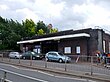 A brown-bricked building with a rectangular, dark blue sign reading "UPNEY STATION" in white letters all under a light blue sky with white clouds