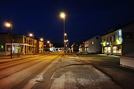 Foto einer von Straßenlaternen beleuchteten Straße, die von einigen Geschäften gesäumt ist.