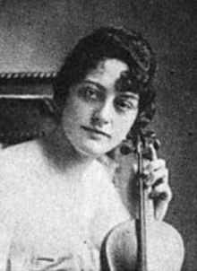 A young woman with light skin and dark hair, holding a violin