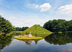 Pyramidensee mit Blick auf die Seepyramide, Begräbnisstätte Fürst Pücklers. Pückler ließ für den Landschaftspark Branitz Seen und Kanäle ausheben und aus dem Aushub Hügel modellieren, sodass aus der flachen Ebene ein Relief entstand. Im Jahr 1856 ließ er hier die Seepyramide, von ihm Tumulus genannt, als seine Grabstätte anlegen. Unweit davon befindet sich Pücklers auf einem künstlichen Hügel errichtete Landpyramide.[16]