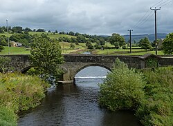 A stone bridge straddling a river with two spans shown in the image, and one pier in the water