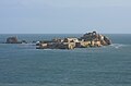 Zdjęcie przedstawia twierdzę Elizabeth Castle na wyspie L'Islet niedaleko portu w Saint Helier. Na wysepce znajdują się kamienne zabudowania oraz fortyfikacje. W tle zdjęcia, po horyzont widać morze.