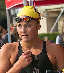 Katie McLaughlin trägt einen schwarzen Badeanzug und eine Gelbe Bademütze. Die Schwimmbrille hat sie auf die Stirn hochgeschoben.