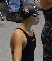 Huske im schwarzen Badeanzug, mit Schwimmbrille und mit schwarzer Badekappe. Auf der Badekappe ist der weiße Nadelbaum auf kardinalrotem S erkennbar, das Emblem des Sportteams der Stanford University.