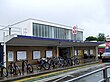 A brown-bricked building with a rectangular, dark blue sign reading "WEST RUISLIP STATION" in white letters all under a light blue sky