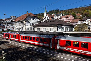 Red and white train at a train station next to a station building