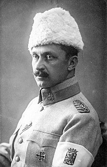 A studio-style picture of General Mannerheim, commander-in-chief of the White Army. He is looking away with his left shoulder turned towards the camera. On his left arm, an armband shows the coat of arms of Finland.