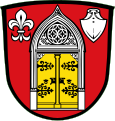 Gemeinde Lohkirchen In Rot ein silbernes neugotisches Portal mit zwei goldenen Türflügeln mit schwarzen Beschlägen, beseitet oben links von einer silbernen heraldischen Lilie, oben rechts von einer silbernen Pflugschar.