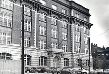 Five story brick and terra cotta building with parking lot and city street in the foreground