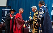 Sadoway, wearing a red robe, on a stage with other men wearing academic regalia