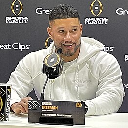 A football coach speaks in front of a microphone.