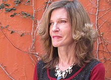 Portrait of lady looking off camera left, wearing necklace. Stands in front of red wall.