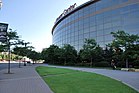 The wide, convex facade of a glassy sports arena and the sidewalk, lawn, and lampposts in front of it. The words "Xcel Energy Center" sit in red atop the stadium.