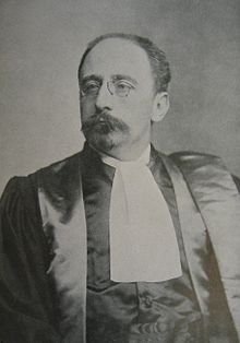 old black and white photo of a man in a black dinner jacket, with a moustache and glasses