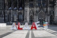 Vor der Fassade des Kölner Doms sind rote und weiße, ca. 1,50 m hohe Buchstaben aufgestellt, die das Wort „Alaaf“ bilden.