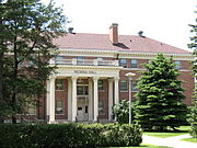 A photograph of the front of a columned building, surrounded by trees