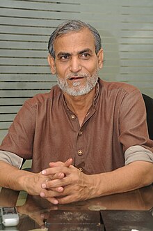 Pervez Bilgrami wearing a brown shirt with rolled-up sleeves, looking left of camera