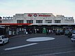 A white-bricked building with a sign reading "Wimbledon" in red letters and people walking in front all under a light blue sky with white clouds