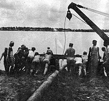 GIs and Indian laborers launch a pontoon on the Hooghly River. Two pontoons lashed together will float pipe to the opposite bank. The main portion of the pipeline will then lie along the river's bottom.