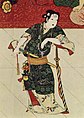 Okuni mit Katana unterm Arm beziehungsweise am Gürtel, weißem Kruzifix um den Hals und diversem Schmuck am dunkelgrün-beigenen Kimono