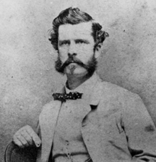 Photograph of a man, seated, in a suit and wearing a bow-tie