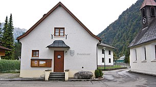 Gemeindeamt in der Gemeinde Stallehr, Vorarlberg. Rechts vor dem Gemeindeamt ein Steinbrunnen und daneben die Wallfahrtskirche.