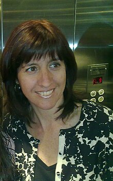 Smiling woman with brown hair, wearing a black blouse and a black and white sweater.