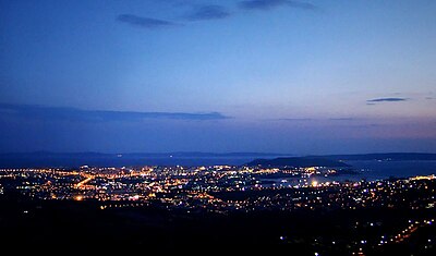 In view from the fortress towards Split at night, there is dark blue sky, and city lights below.