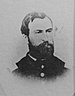 Head of a white man with a full beard and receding hairline, wearing a military jacket with large bright buttons.