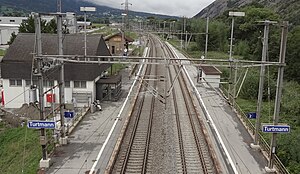 Double-tracked railway line with two-story gabled-roof building at left