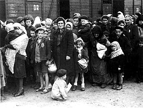 Γυναικόπαιδα μπροστά από βαγόνι τρένου εμπορευμάτων, διακρίνονται στα ρούχα τους αστέρι με το οποίο σημαδεύονταν οι Εβραίοι.