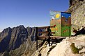 ein buntbemaltes Toilettenhäuschen über einem Abhang mit Blick über die Hohe Tatra