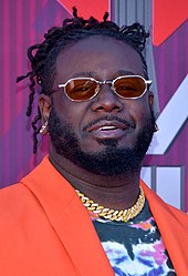 T-Pain in an orange coat, wearing a gold chain and aviators