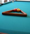 Racking up a game of three-ball, in triangle formation, using the standard large triangle rack more commonly used for eight-ball and straight pool. In this example, the 2 ball is on the foot spot. (Expansive-view version.)