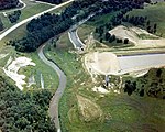 A stream flowing through a rural area of woods and fields with a dug channel to the right