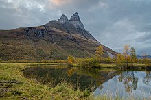 Foto eines Flusses, an dessen Uferseite sich ein Berg mit zwei Spitzen erhebt