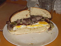 A steak and egg sandwich with bacon and cheddar cheese