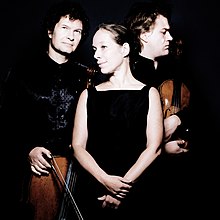 Photo of a woman standing between a man holding a cello and a man holding a violin