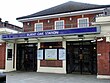 A red-bricked building with a blue sign reading "BURNT OAK STATION" in white letters and four surveillance cameras in front of the doors