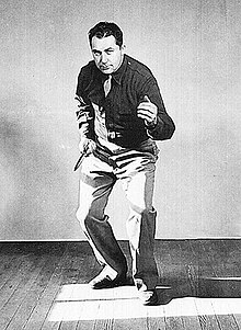 Black and white image of Rex Applegate in military uniform. He is facing the camera, slightly crouched, fighting knife in right hand and with left hand in a ready position about mid-chest high.