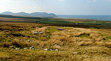 The Behy court tomb looking west across Broadhaven Bay. The capstone of the chamber is visible; however, the majority of the monument is buried beneath a layer of peat.