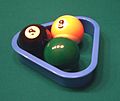 Racking up a game of three-ball, in triangle formation, using a miniature triangle rack specifically for three-ball. In this side-view example, the 8 ball is on the foot spot, and this is a practice-game rack — the 8 and 9 are used because they are the intimidating "money balls" in two popular games, while the 6 is used because it is the hardest to see on the green baize.