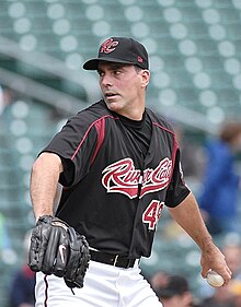 A man in a black baseball jersey and cap with white pants